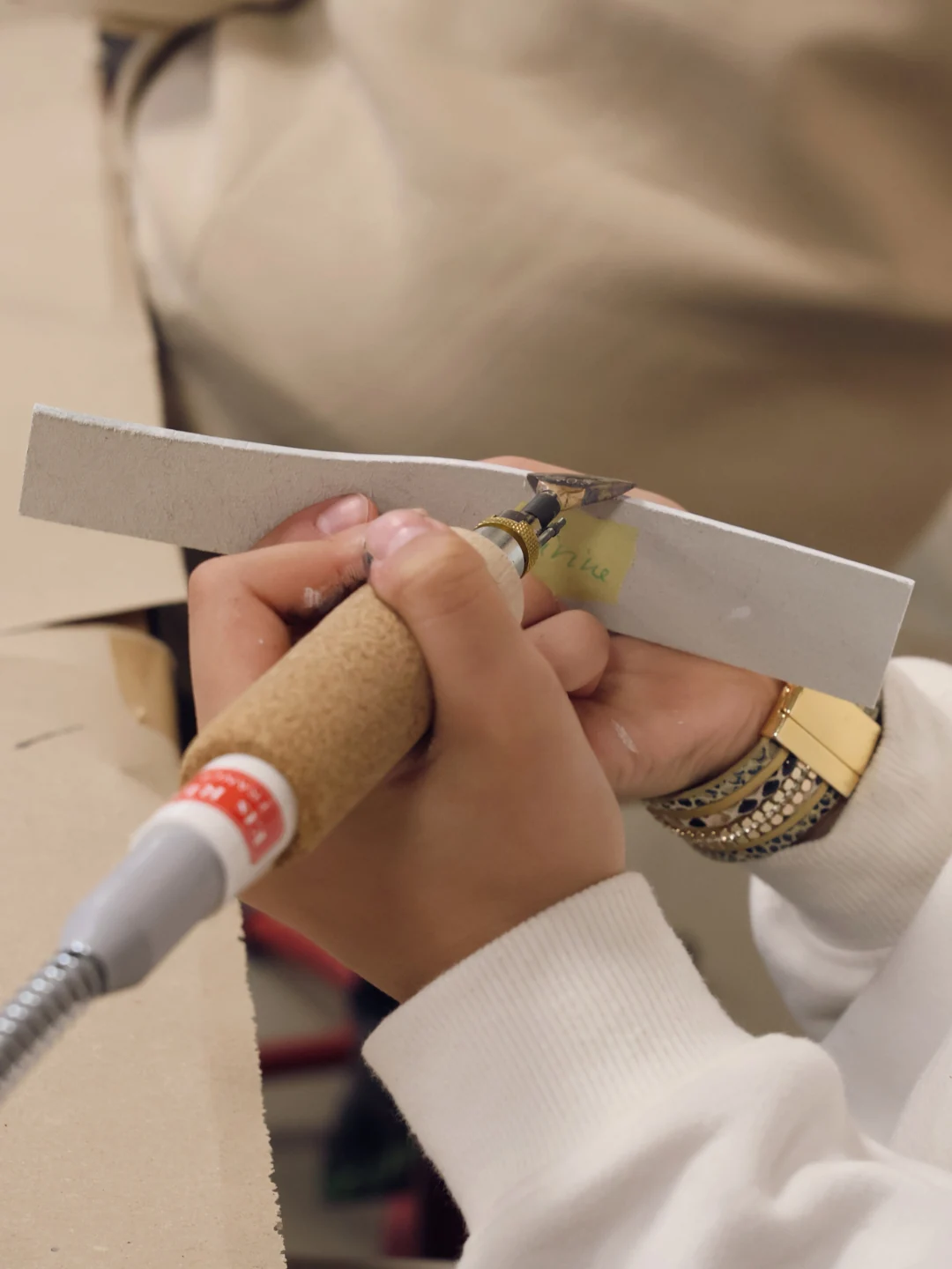 Gros plan sur les mains d'un élève appliquant une finition sur la tranche d'une ceinture en cuir à l'aide d'un fer à fileter lors d'un atelier.